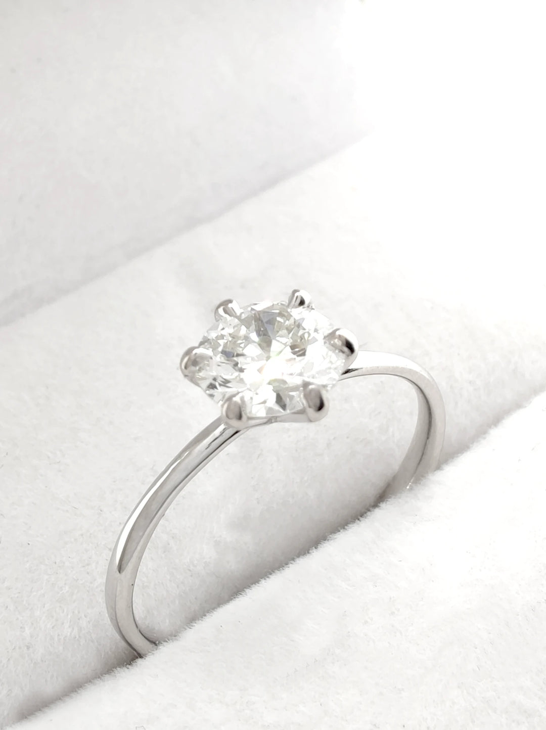 An elegant solitaire diamond ring in 18K white gold, displayed on a soft white fabric background to emphasize its luminous center stone and refined design