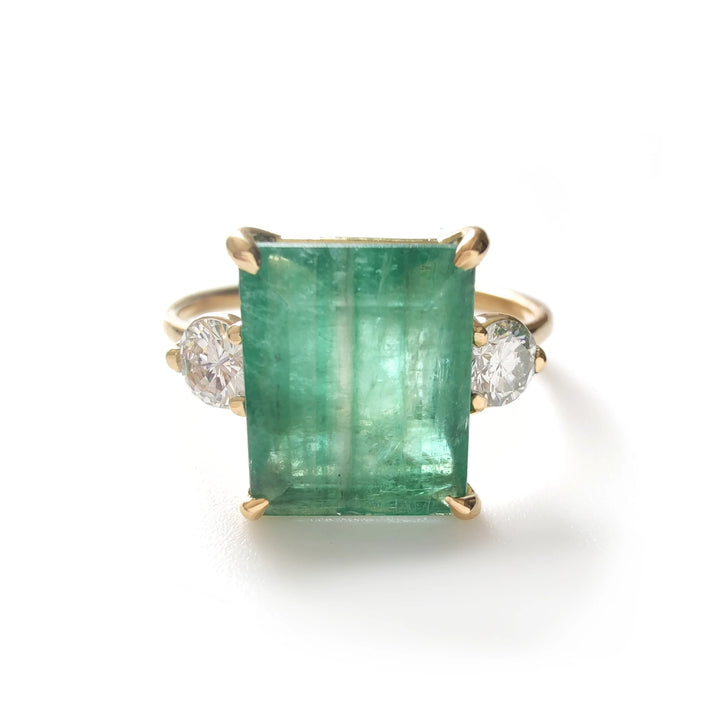 Front view of 18K yellow gold three-stone ring with emerald cut emerald and side diamonds