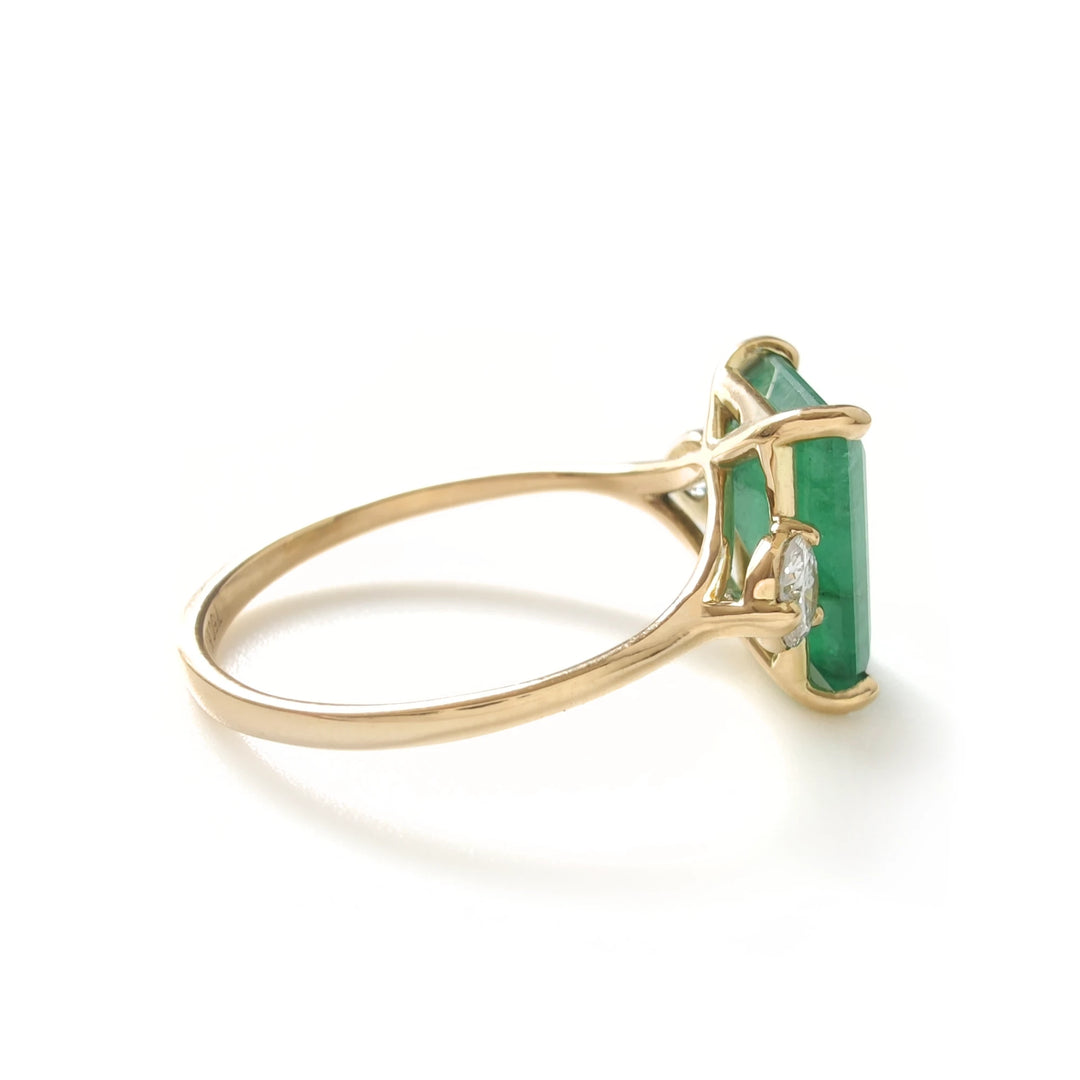 Right angle of three-stone ring showing emerald and diamond setting in yellow gold