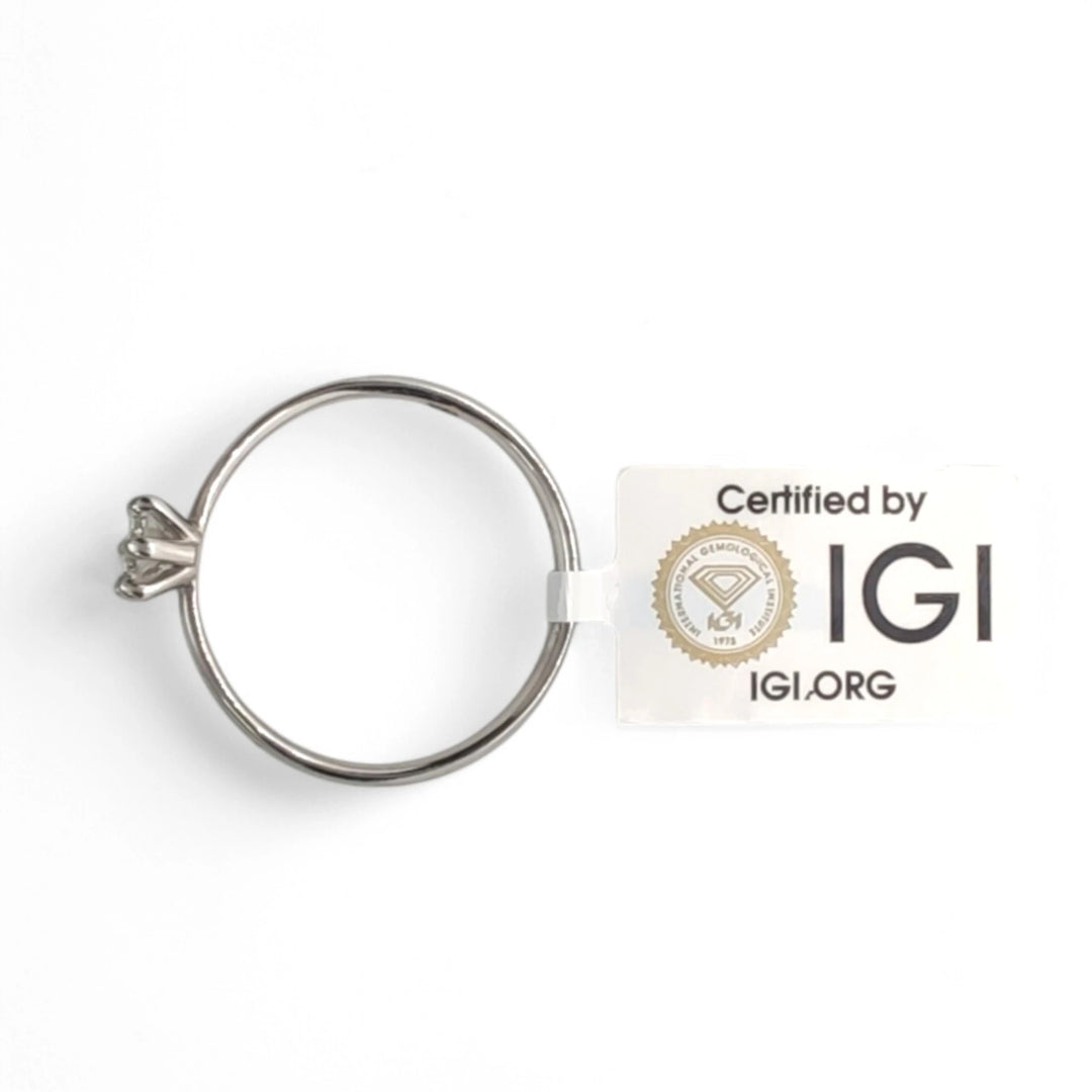 The platinum solitaire ring displayed alongside its IGI certification card, emphasizing authenticity. The secure six-prong setting and polished band are showcased against a clean white background, with the IGI logo prominently featured