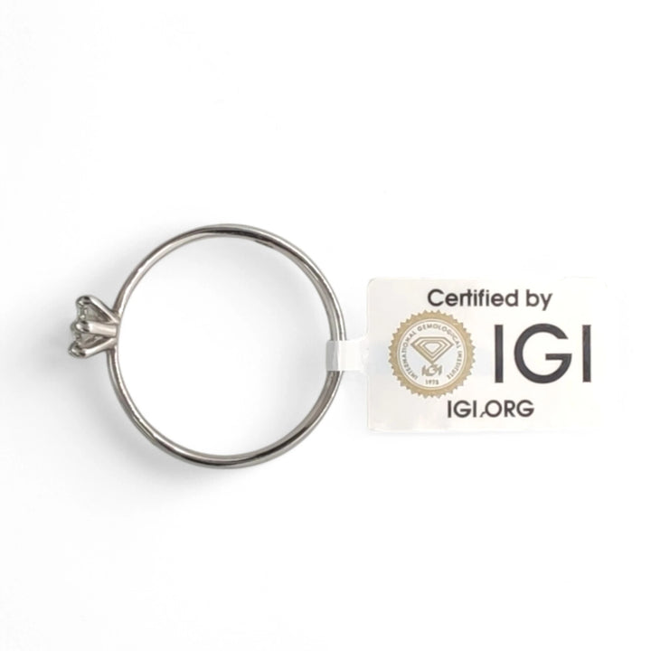 The platinum solitaire ring displayed alongside its IGI certification card, emphasizing authenticity. The secure six-prong setting and polished band are showcased against a clean white background, with the IGI logo prominently featured