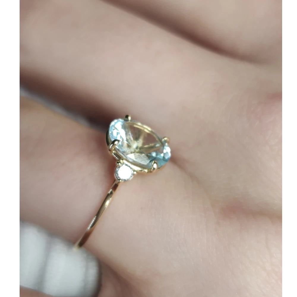 Close-up of a women’s 18K yellow gold three-stone ring with an oval aquamarine and diamond accents