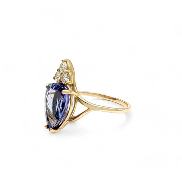 Left side view of a 14K yellow gold engagement ring showcasing a pear-cut tanzanite and three brilliant diamonds, emphasizing the ring's elegant design and craftsmanship