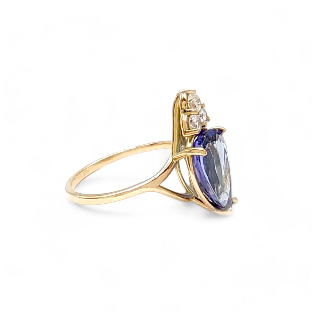 Right side view of a 14K yellow gold ring with a central pear-cut tanzanite and three diamonds, showcasing the ring's sleek and elegant design