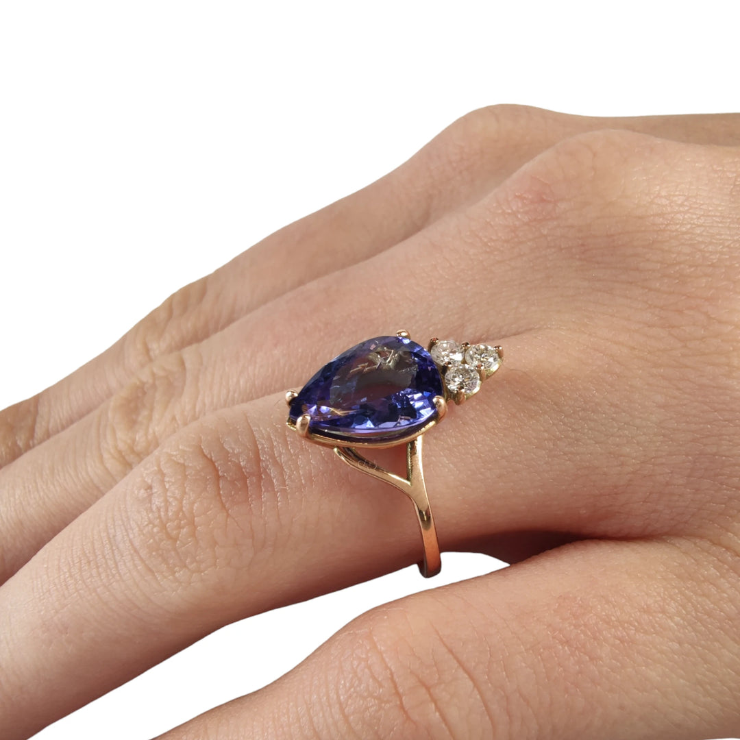 View of a model's finger adorned with a 14K yellow gold engagement ring featuring a pear-cut tanzanite and three brilliant diamonds, highlighting its suitability as a special engagement or Christmas gift.
