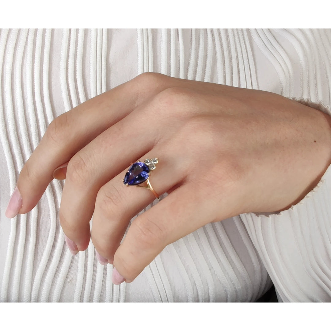 Third pose of a model's hand featuring a 14K yellow gold engagement ring with a pear-cut tanzanite and three diamonds, showcasing the ring's artistic and handmade quality