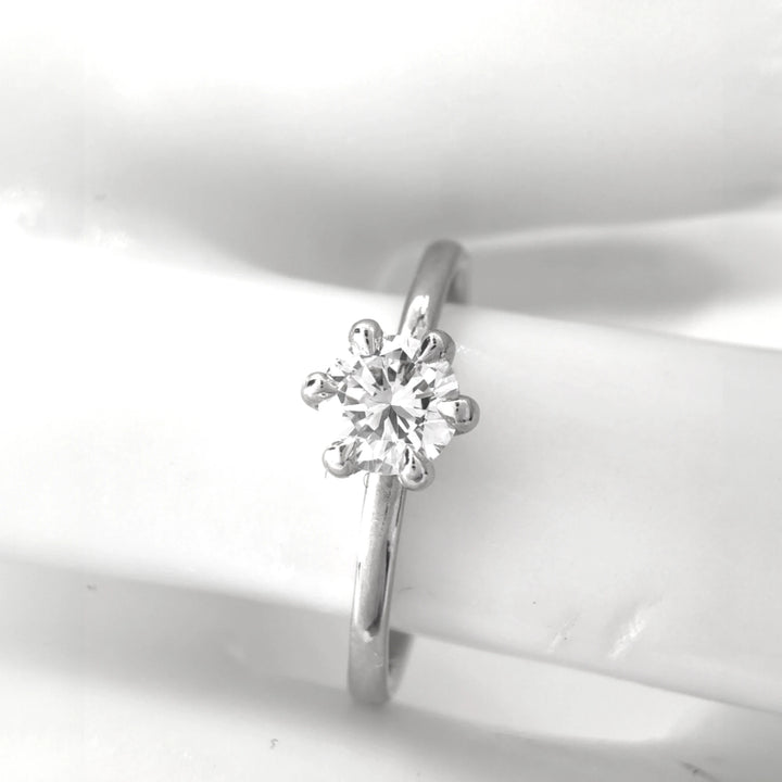 A classic solitaire engagement ring featuring a round brilliant-cut diamond held securely by six elegant prongs. The sleek platinum band gleams under soft lighting, showcasing the stone’s brilliance against a pristine white backdrop