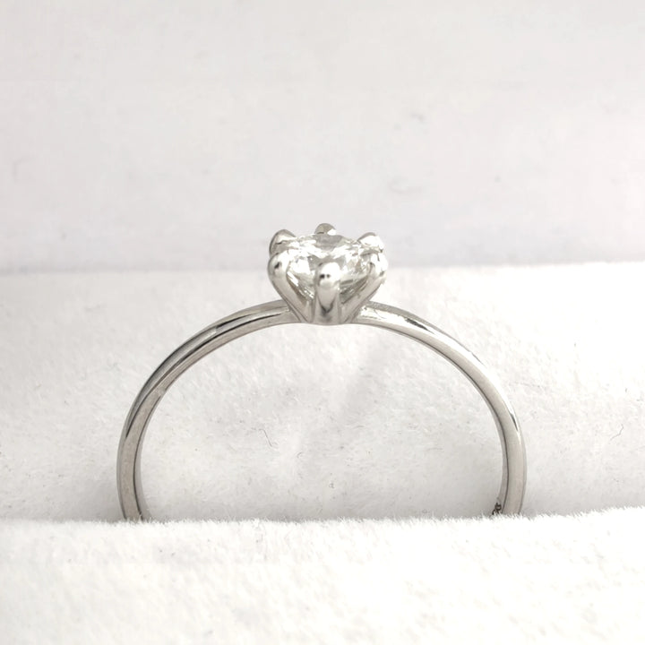 The ring displayed from a side angle, emphasizing its slender platinum band and the secure six-prong setting that cradles the sparkling diamond. The soft white fabric background enhances the ring’s luminous quality