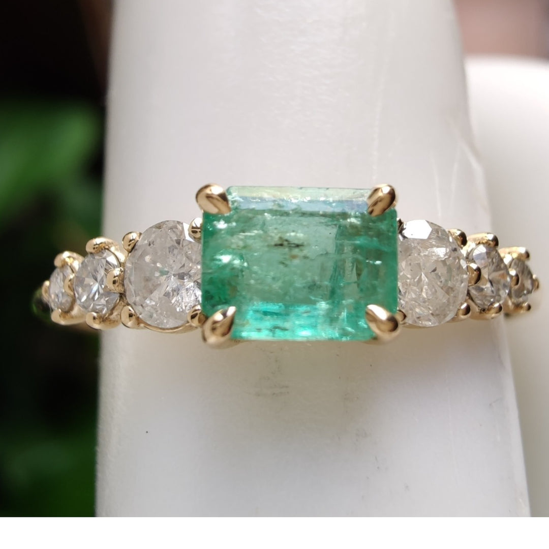 Close-up detail of a stunning 18K yellow gold ring with a central emerald and three diamonds on each side displayed on a mannequin finger