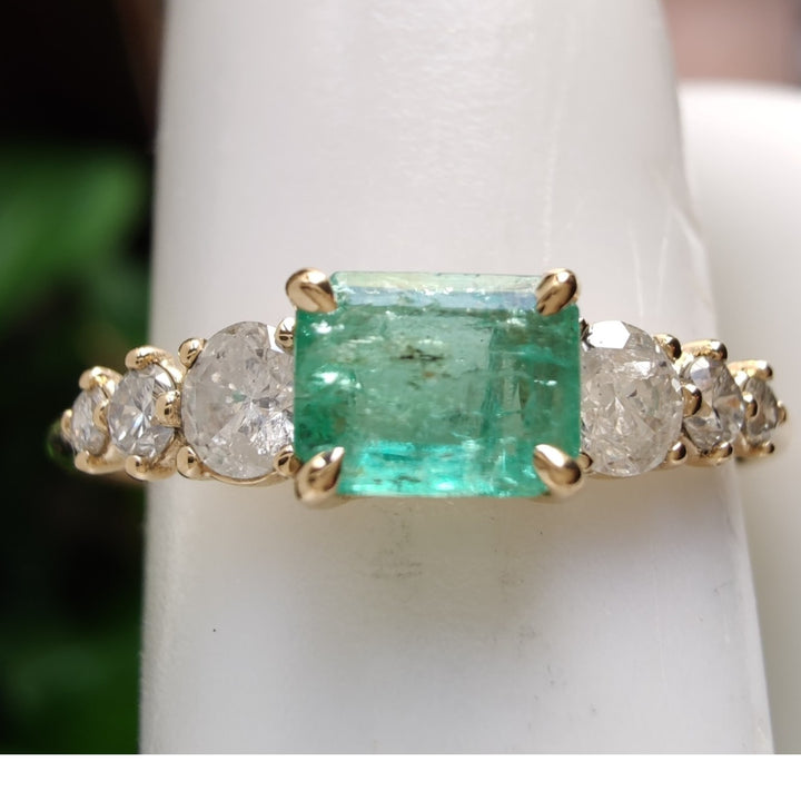 Close-up detail of a stunning 18K yellow gold ring with a central emerald and three diamonds on each side displayed on a mannequin finger