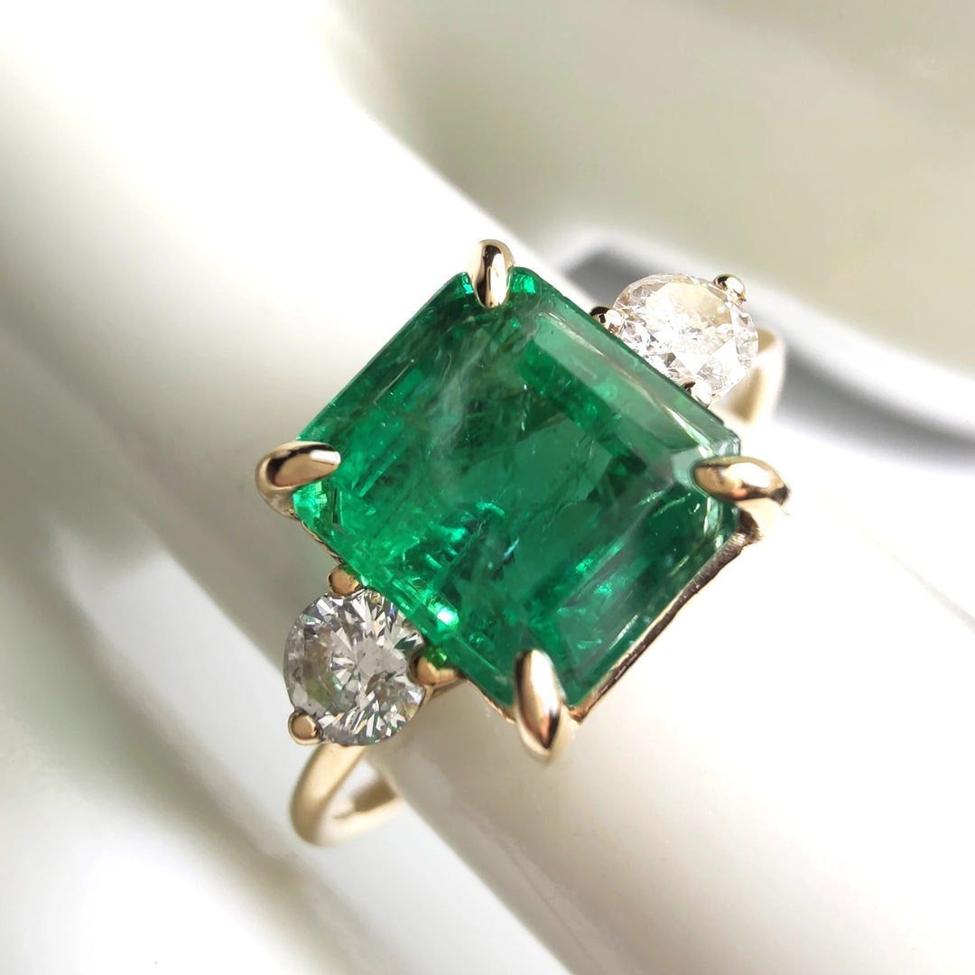 Close-up of a womenβs three-stone ring in 18K yellow gold with an emerald cut emerald and diamond side stones