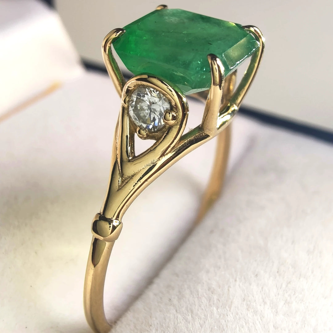 Side view of a contemporary three-stone engagement ring in 18K yellow gold with a central octagon emerald and diamonds