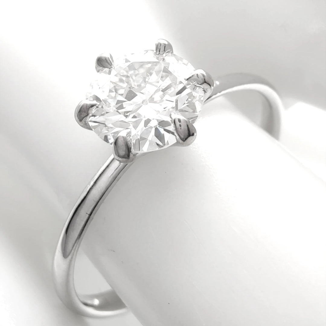 Classic six-prong solitaire engagement ring in 18K white gold, showcasing a fiery round brilliant diamond, elegantly displayed on a glossy white ceramic finger model