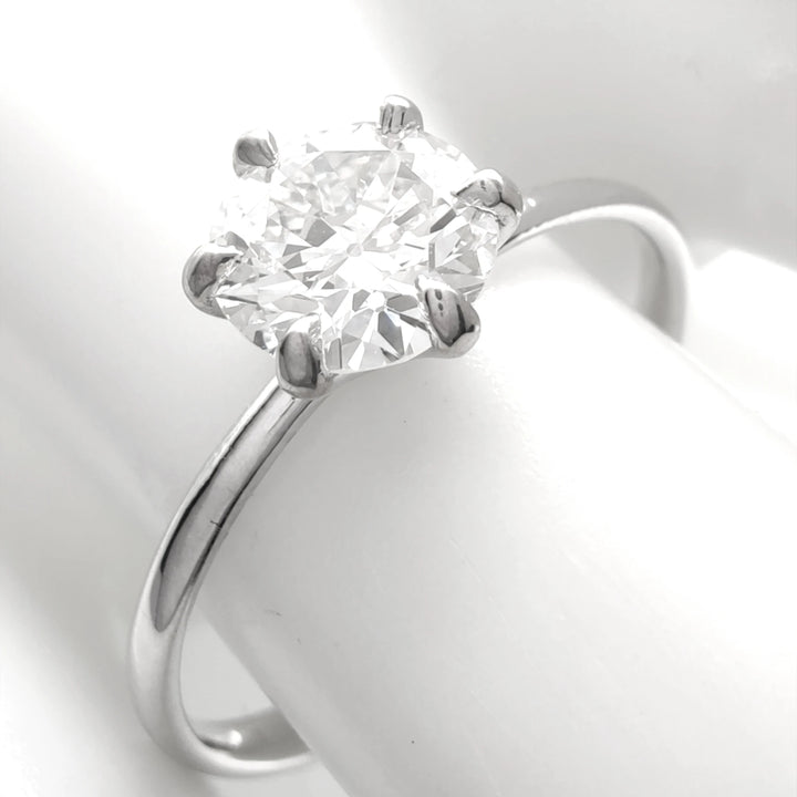 Classic six-prong solitaire engagement ring in 18K white gold, showcasing a fiery round brilliant diamond, elegantly displayed on a glossy white ceramic finger model