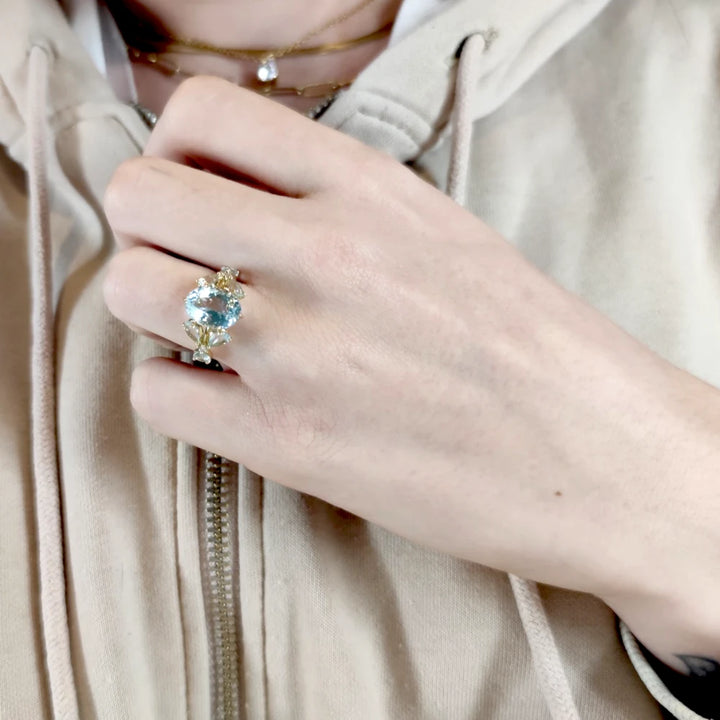 Beautiful engagement or cocktail ring with an oval aquamarine centerpiece and diamond accents displayed on a model’s hand in a different pose