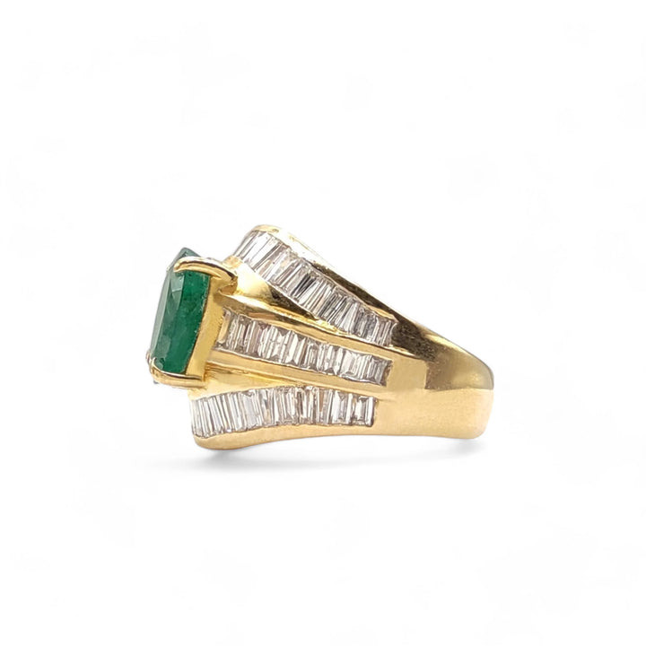 Left side view of a 22K gold cocktail ring featuring a central oval emerald flanked by sophisticated diamond baguette bands, highlighting its intricate design