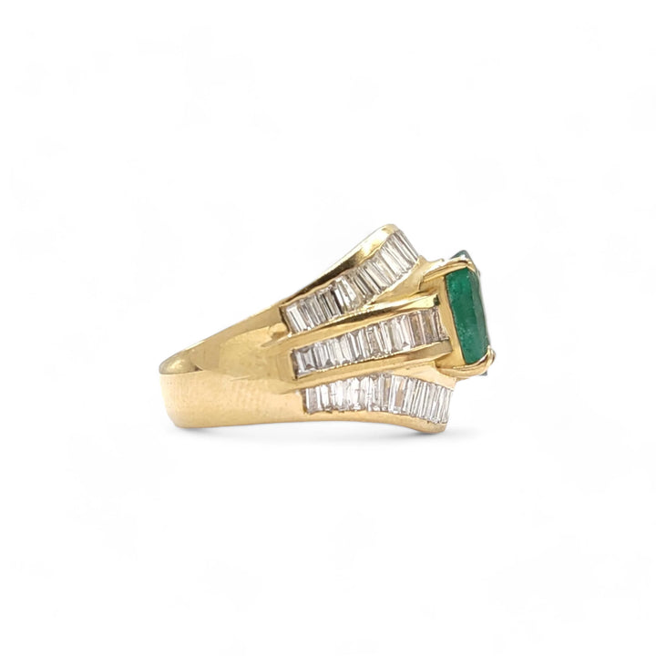 Right side view of a luxurious cocktail ring in 22K gold with an oval emerald and three rows of diamond baguettes, showcasing the ring's exquisite craftsmanship