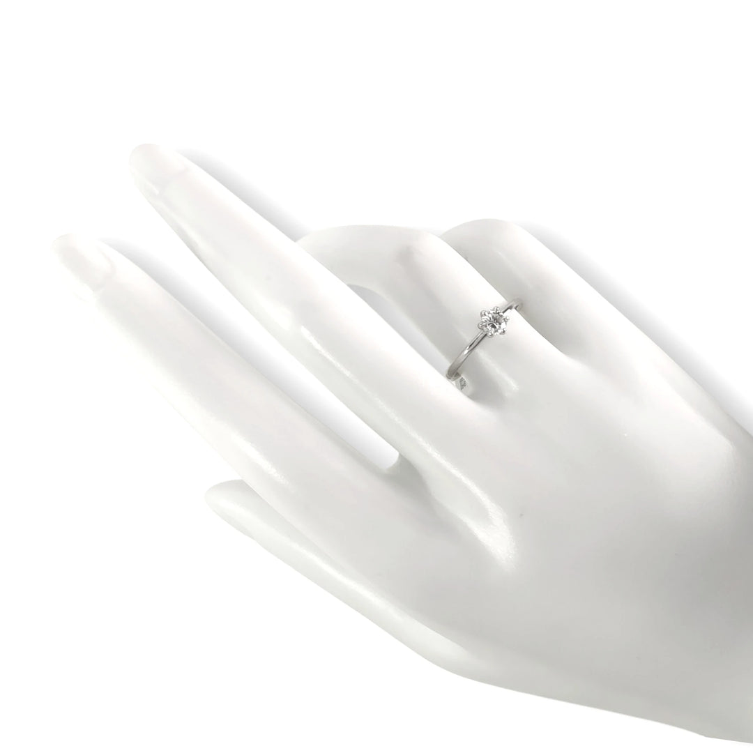 The ring elegantly positioned on a glossy white ceramic hand mannequin, demonstrating how it sits gracefully on the finger. The contrast between the smooth platinum and the lustrous ceramic accentuates its refined design