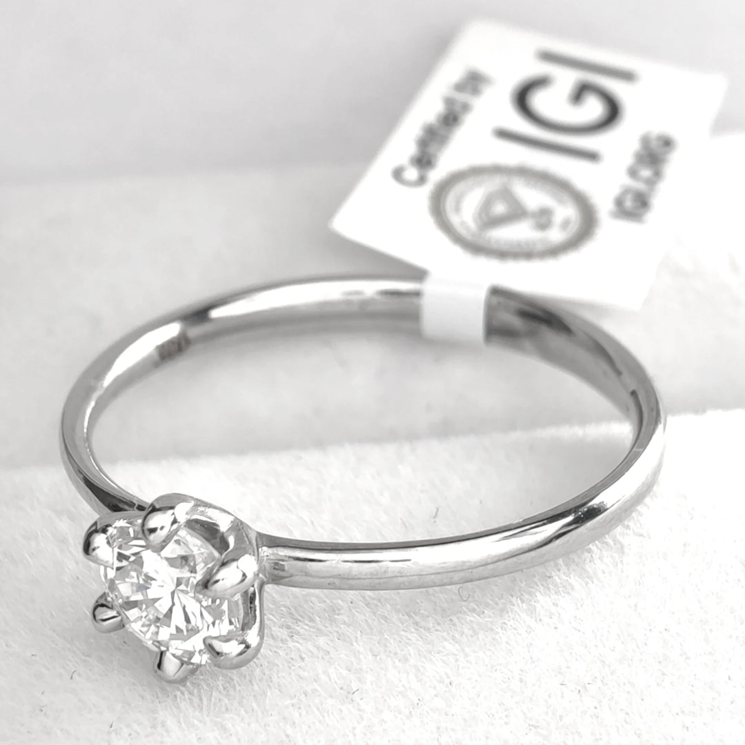 The engagement ring accompanied by an IGI (International Gemological Institute) certification card, verifying the diamond’s authenticity and quality. The ring rests on a textured white surface, with the card partially visible in the background