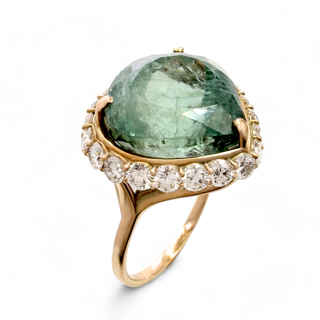 Green tourmaline ring with a halo of diamonds set in gold. The ring showcases the vibrant green hue of the tourmaline, complemented by the sparkling diamonds that surround it, all elegantly mounted on a gold band.