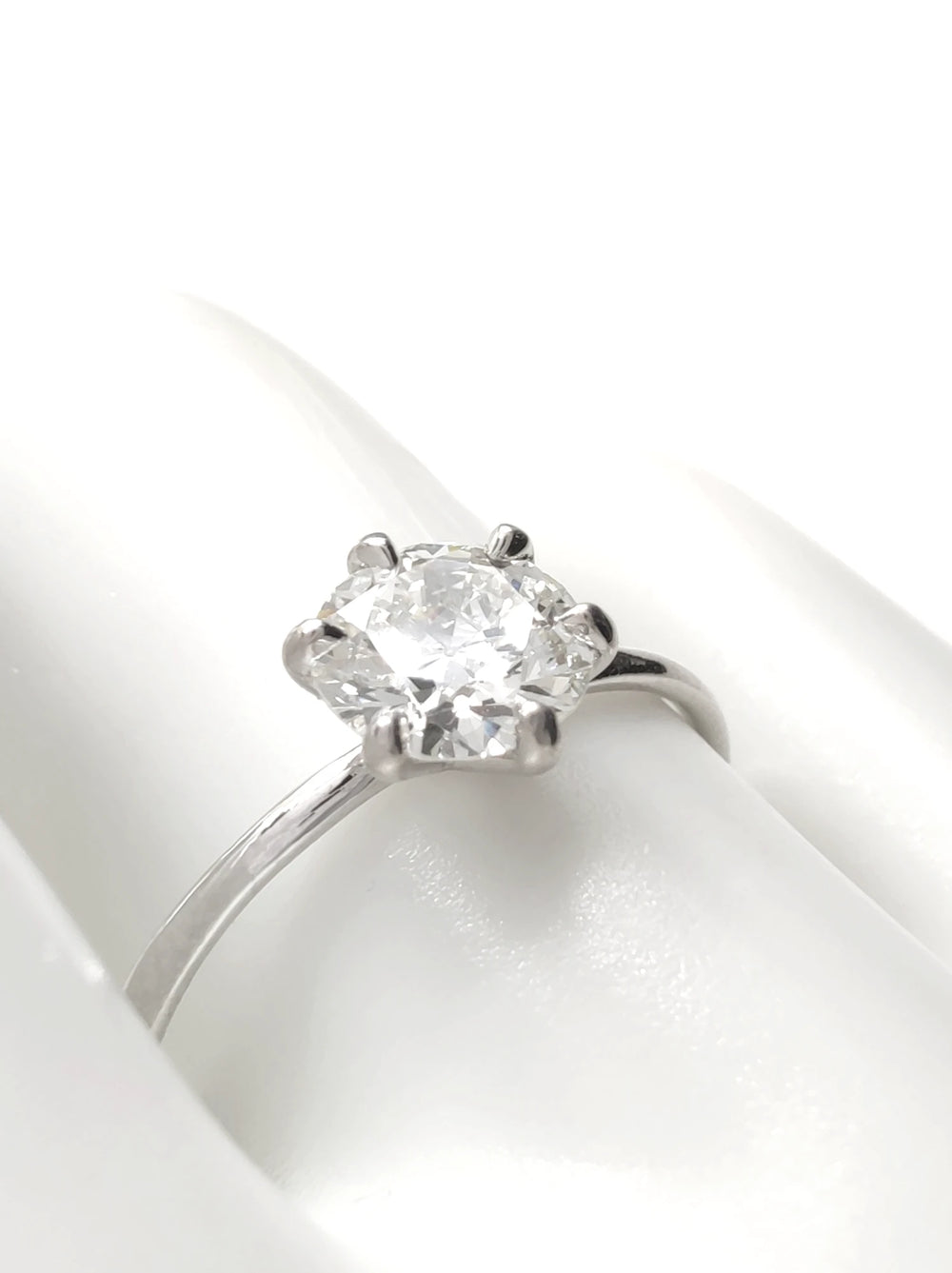 A classic six-prong solitaire engagement ring featuring a round brilliant-cut diamond set in 18K white gold, displayed on a white ceramic finger model.