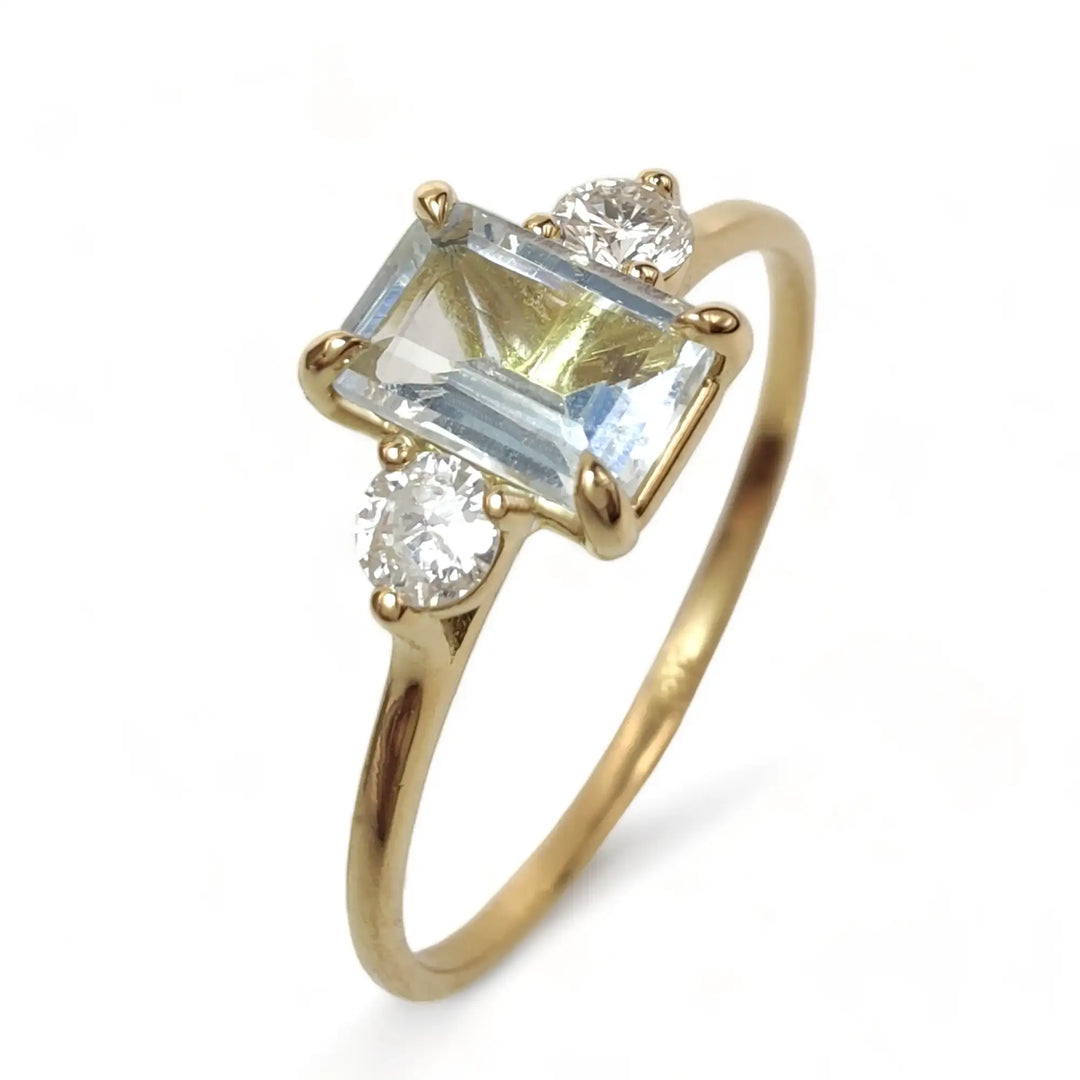 Image of a solid 18K gold three-stone engagement ring for women, featuring a central aquamarine and a diamond on each side, designed for timeless elegance and special occasions