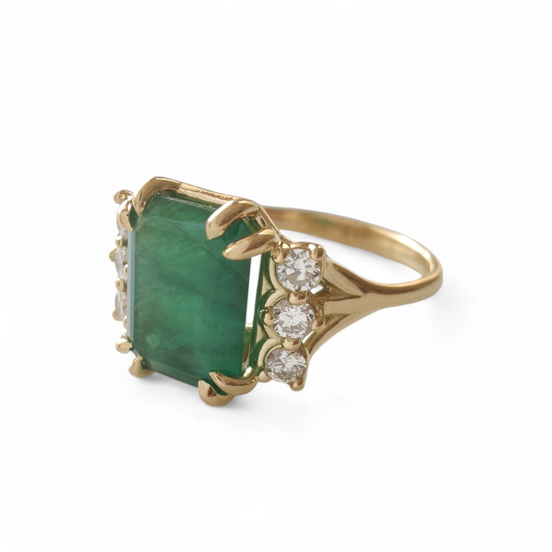 Left side view of a contemporary 18K yellow gold engagement ring featuring a central emerald and three diamonds on each side