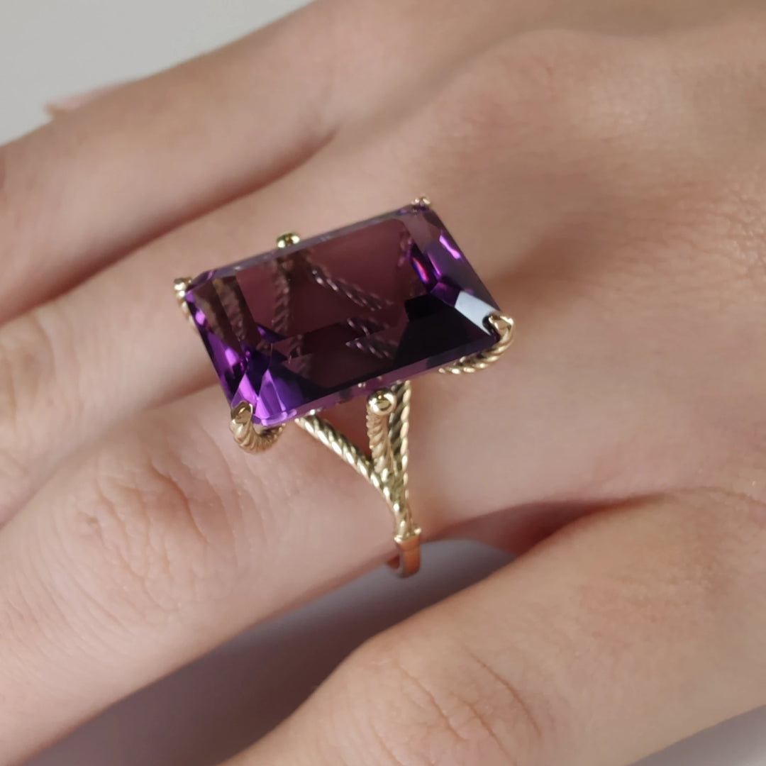 Close-up view of a unique 14K yellow gold ring with a sculptural design, featuring a large amethyst mounted in twisted prongs