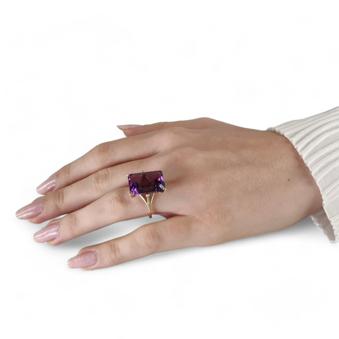 Elegant sculptural ring featuring a large amethyst set in twisted prongs, crafted in 14K yellow gold, worn on a model’s full hand