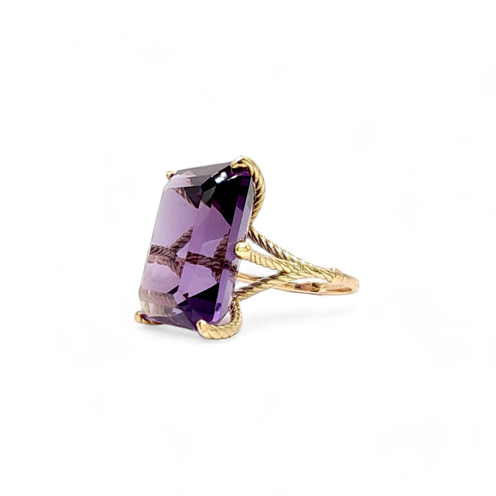 Left side view of a bold and sculptural 14K yellow gold ring featuring a large amethyst in a twisted prong setting

