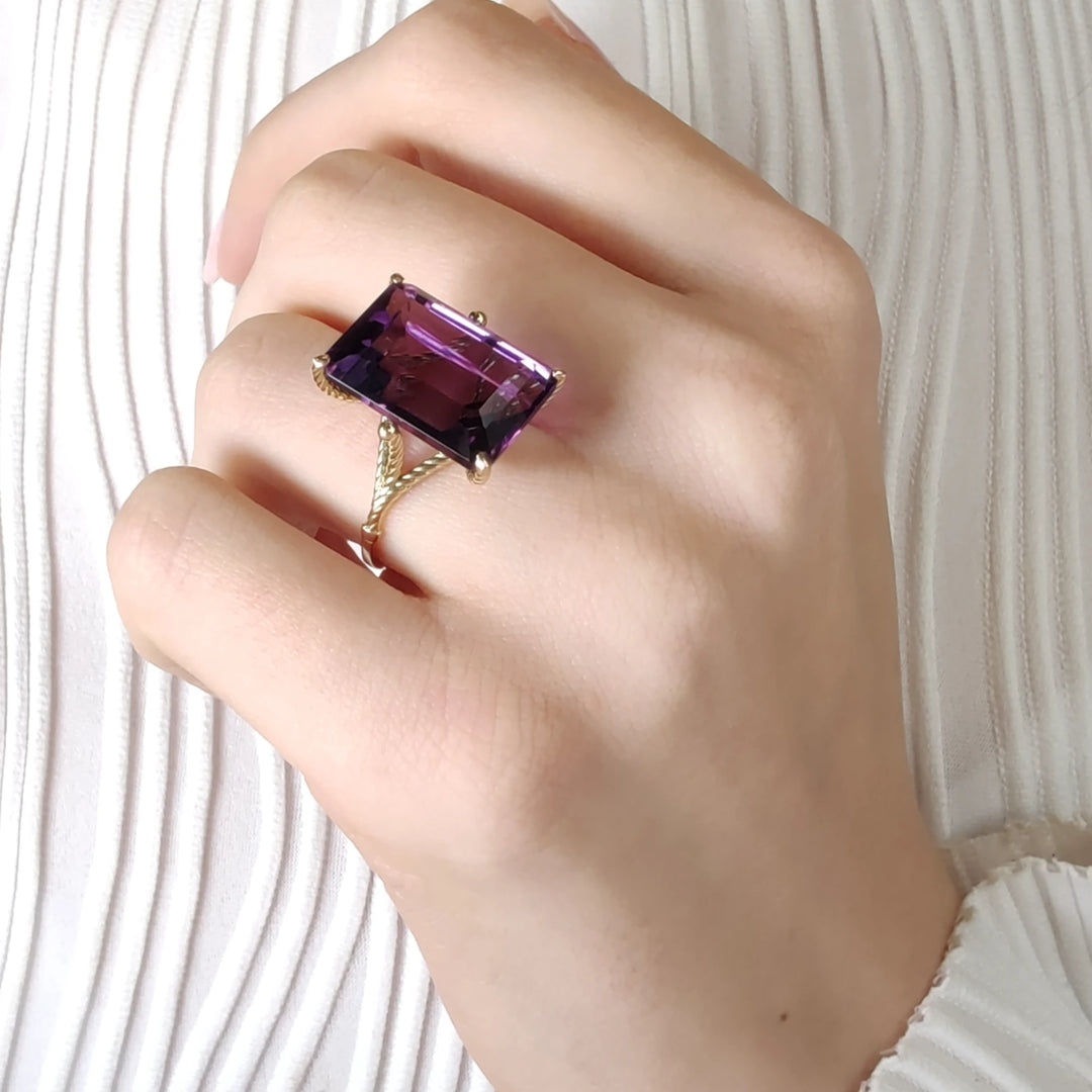 Beautiful 14K yellow gold ring with a large amethyst in twisted prongs displayed on a female model’s hand in an elegant pose