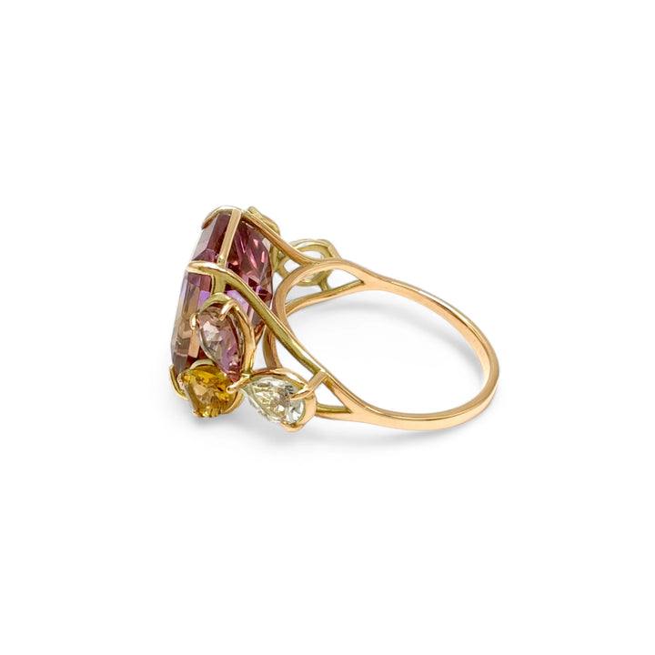 Left side view of a singular cocktail ring in 14K yellow gold with a central ametrine, flanked by pear-shaped amethysts and aquamarines