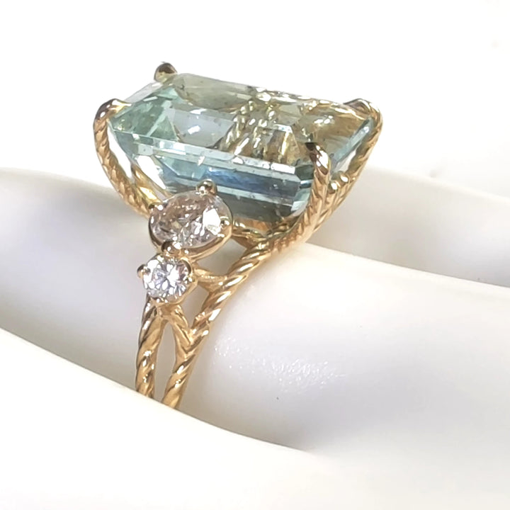 Close-up detail of a 18K yellow gold cocktail ring with an emerald-cut aquamarine and diamond accents displayed on a mannequin finger