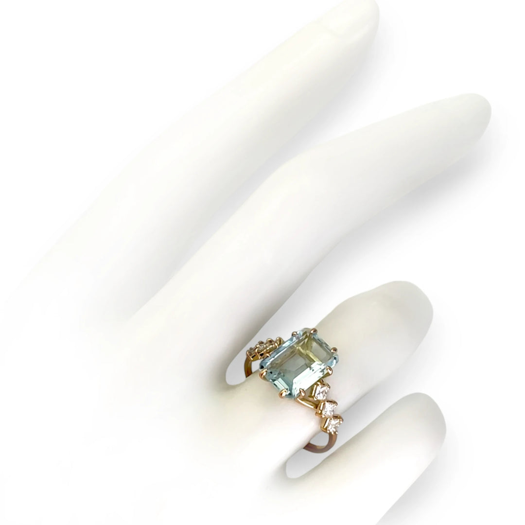 Elegant 14K yellow gold ring with a central aquamarine and princess-cut diamonds, displayed on a white mannequin hand, showcasing its unique craftsmanship