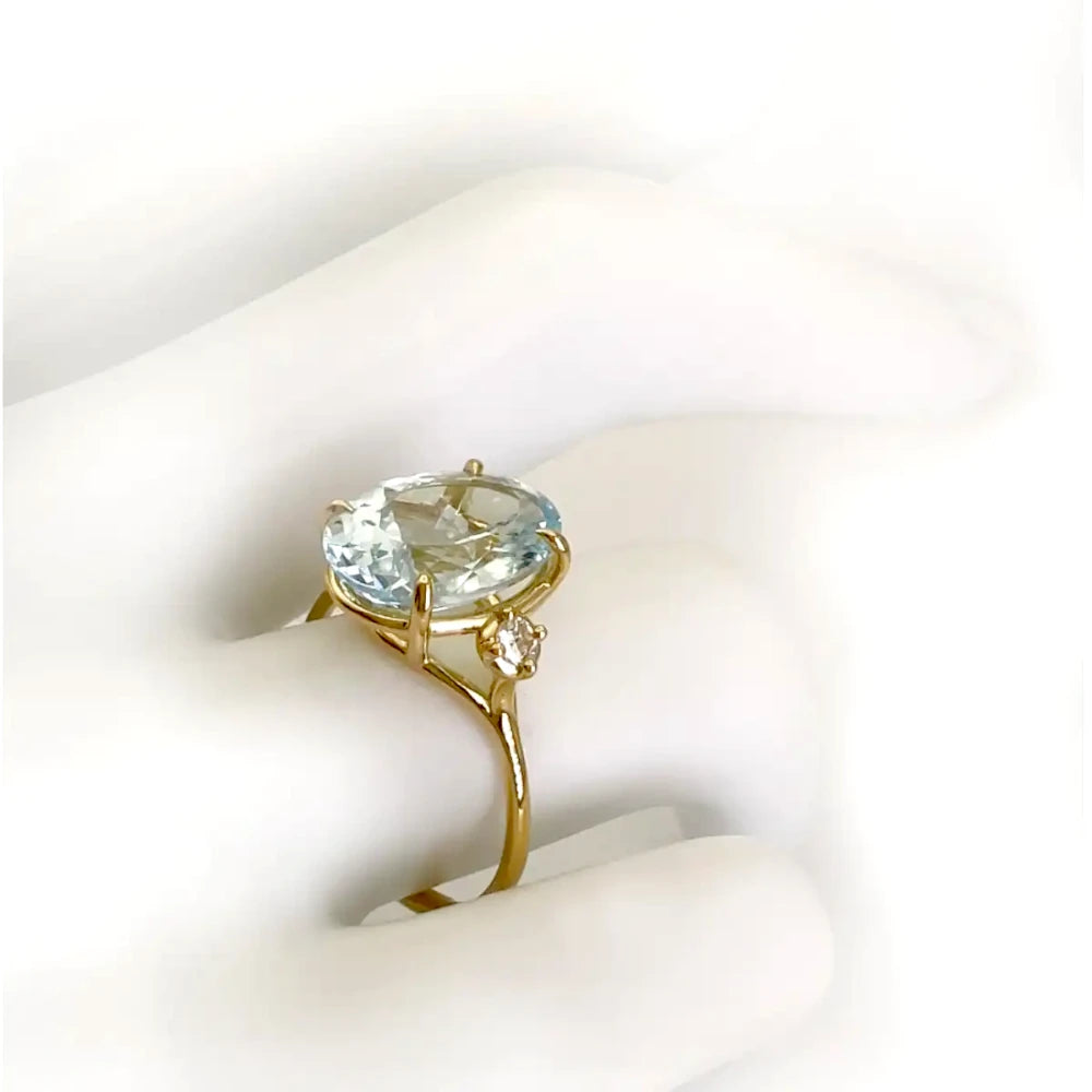 Elegant 18K yellow gold three-stone engagement ring with an oval aquamarine and diamonds, displayed on a mannequin hand