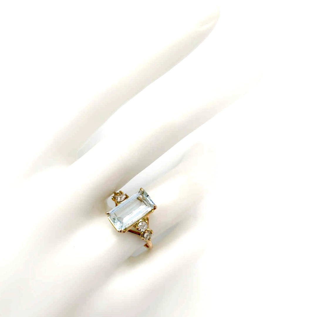 Elegant 14K yellow gold engagement ring with a natural emerald-cut aquamarine and diamond accents displayed on a mannequin hand