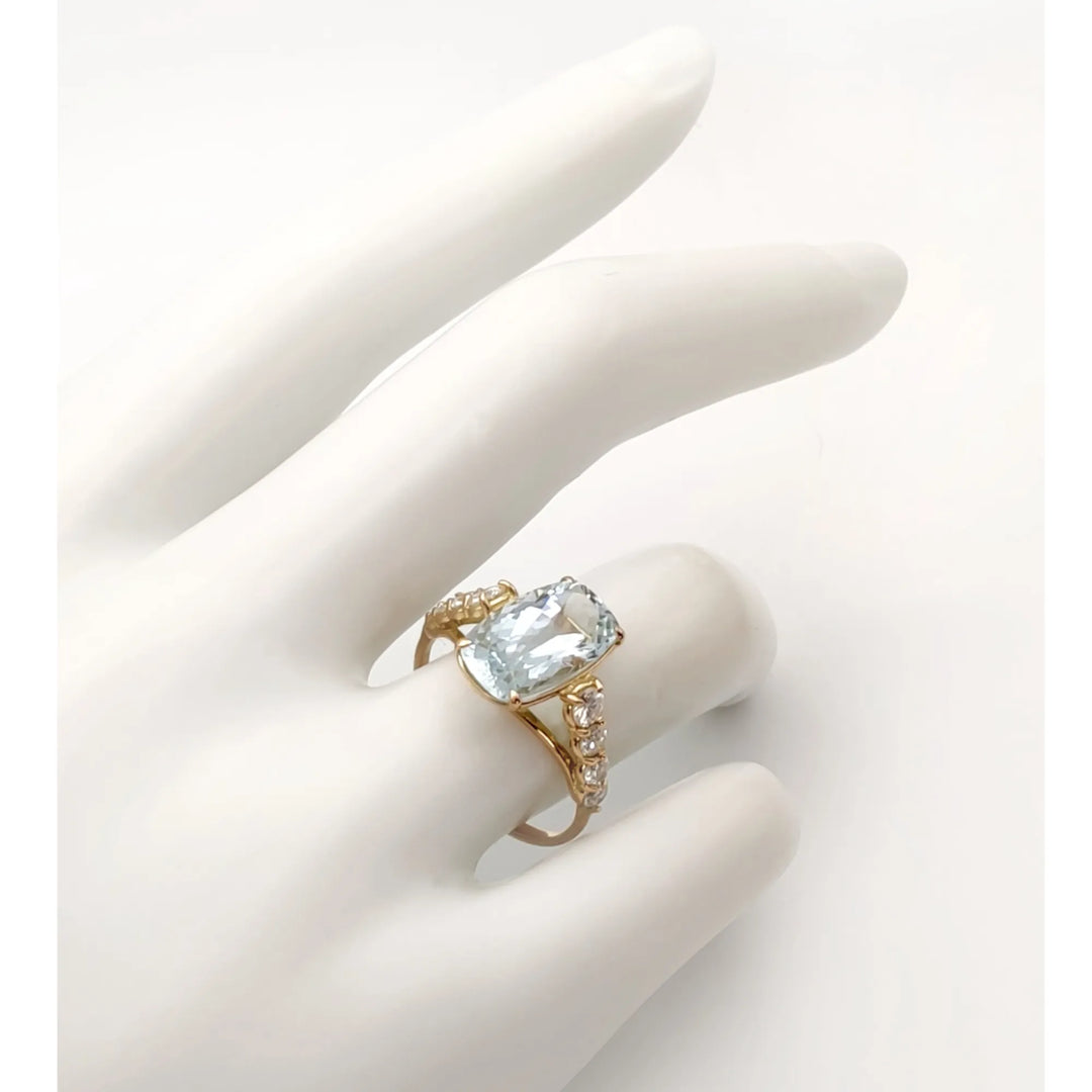 Elegant 14K yellow gold ring with a central cushion-cut aquamarine and diamond accents displayed on a mannequin hand, showcasing its sculptural design