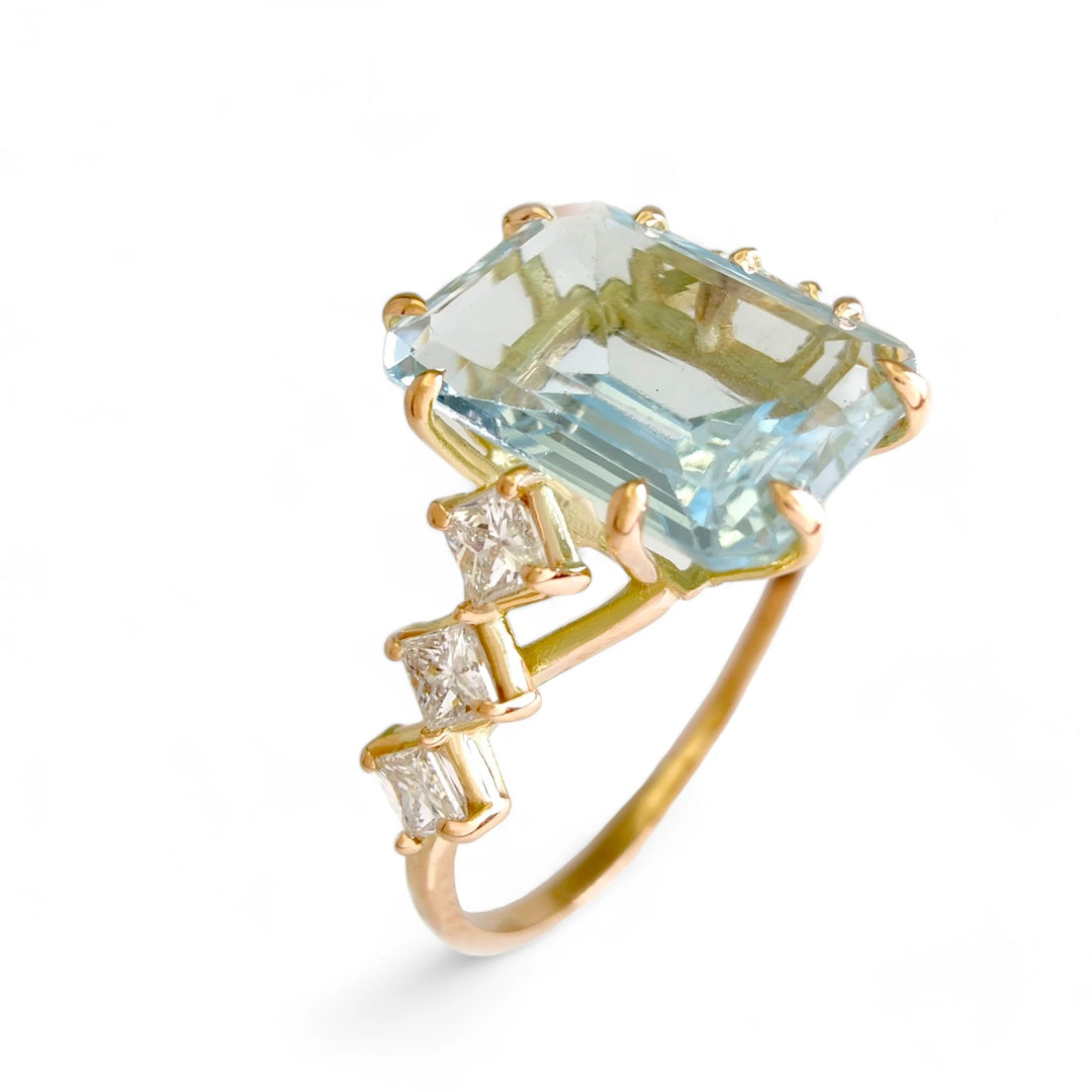 Vertical angled view of a handcrafted 14K solid yellow gold ring featuring a large aquamarine centerpiece with three princess-cut diamonds on each side, perfect for women who value artistic designs