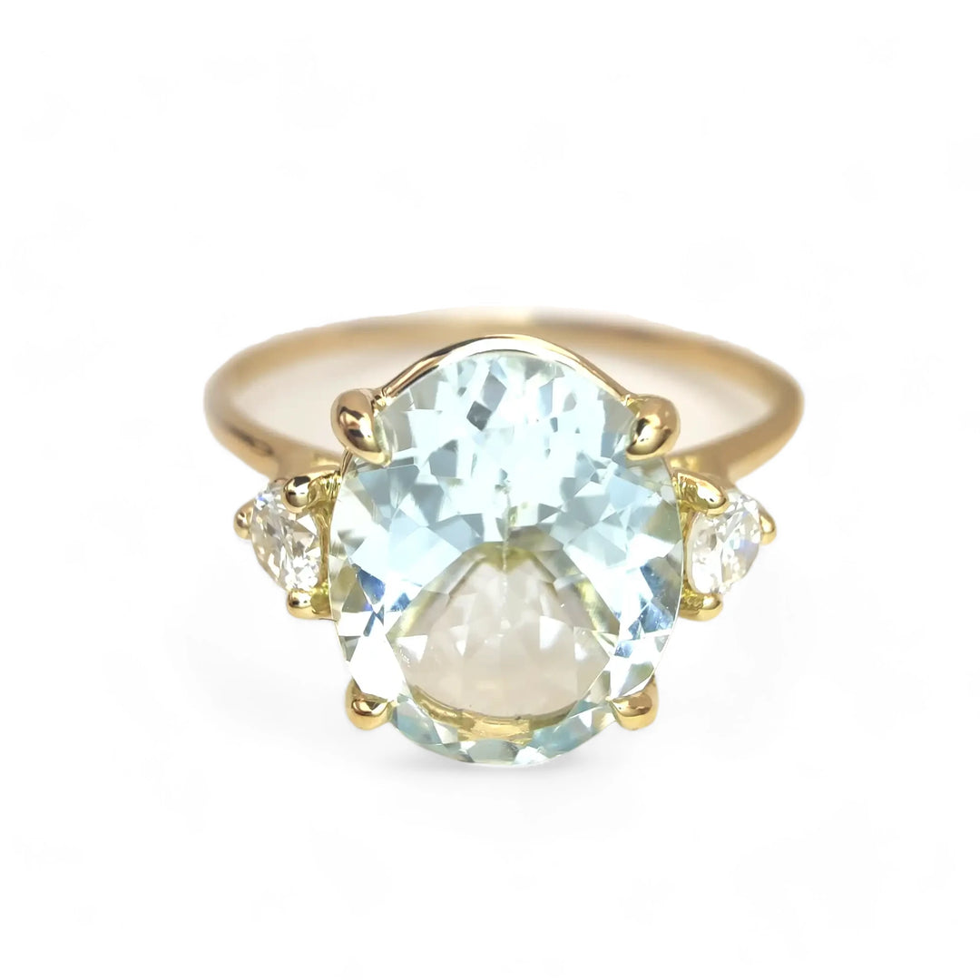 Front view of a three-stone 18K yellow gold women’s ring featuring an oval aquamarine and round diamonds