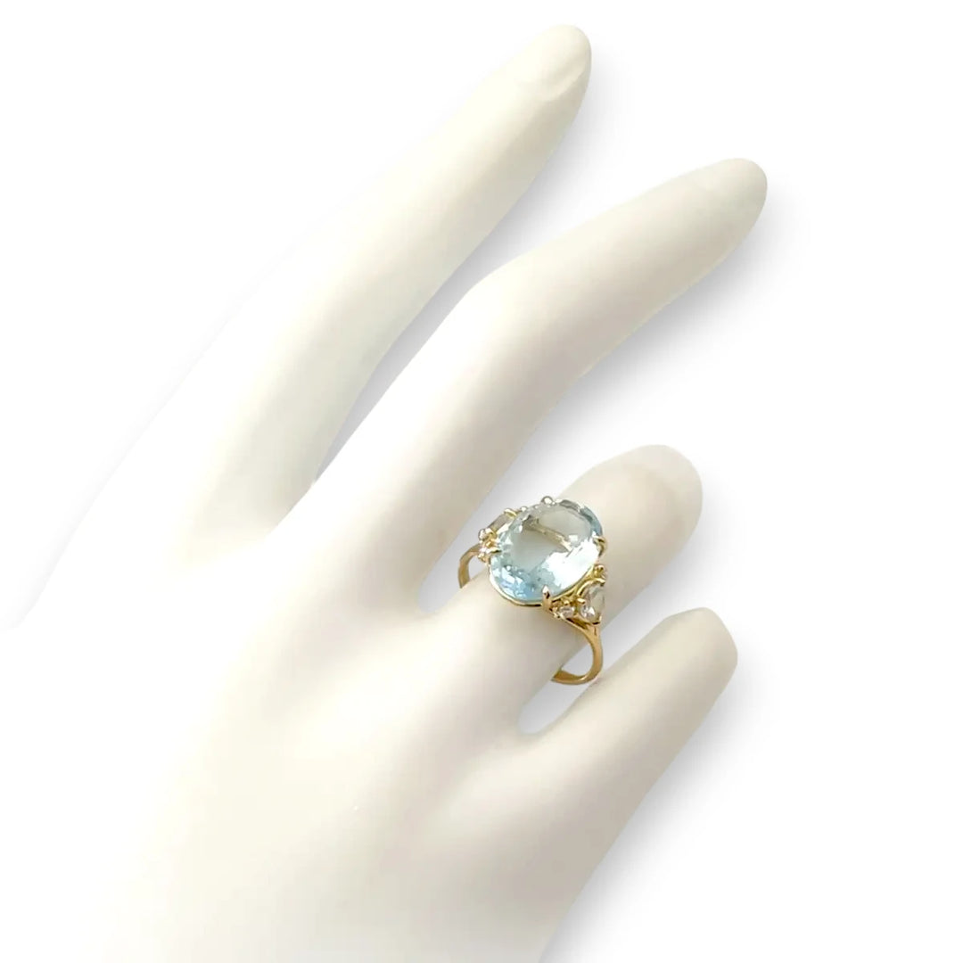 Elegant 18K yellow gold engagement ring with an oval aquamarine, pear-shaped aquamarines, and diamonds displayed on a mannequin’s full hand