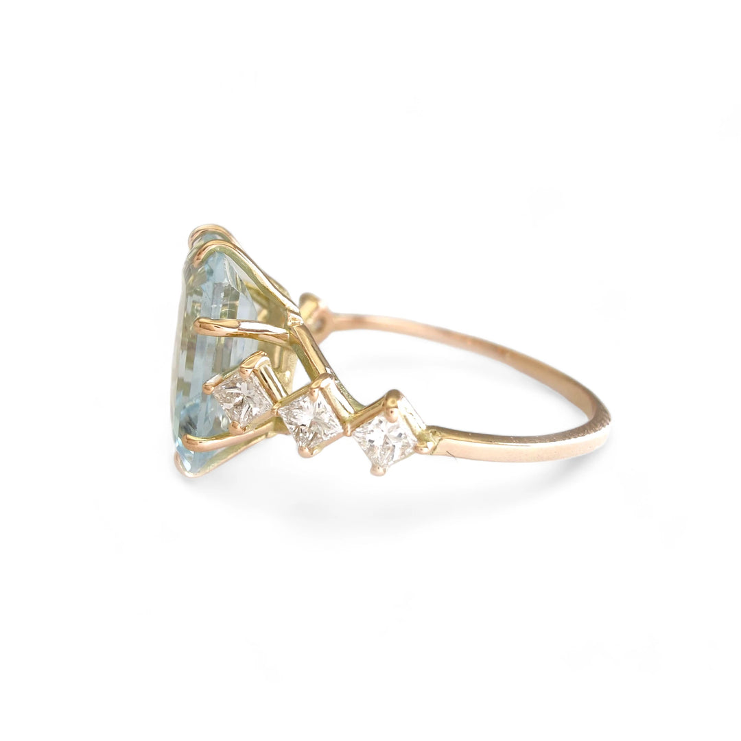 Left side view of a women’s 14K yellow gold ring featuring a large aquamarine centerpiece flanked by princess-cut diamonds