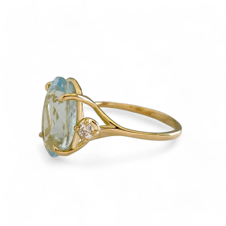 Left side view of a unique 18K yellow gold engagement ring with an oval aquamarine and diamond accents in a three-stone design