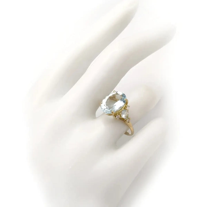 Elegant 18K yellow gold engagement ring with an oval aquamarine centerpiece, additional pear-shaped aquamarine, and diamonds displayed on a mannequin hand