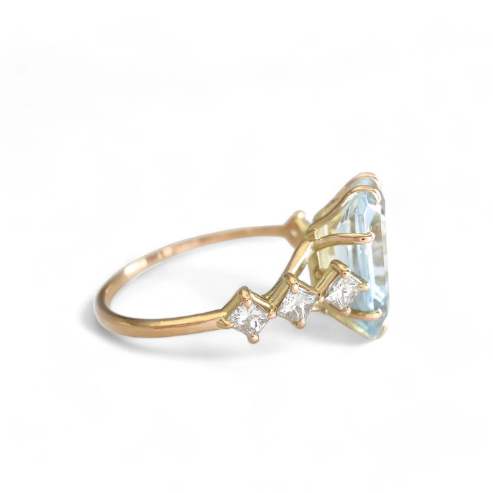 Right side view of a singular 14K yellow gold ring with an aquamarine centerpiece and three princess-cut diamonds on each side