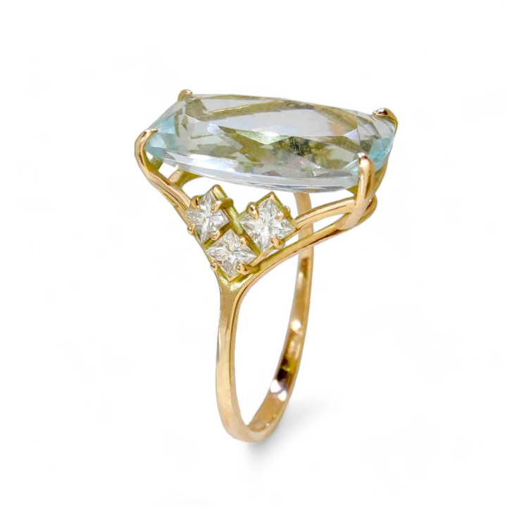 Vertical close-up view of a women’s 14K yellow gold ring featuring a rectangular cushion aquamarine centerpiece with three princess-cut diamonds on each side in a V arrangement