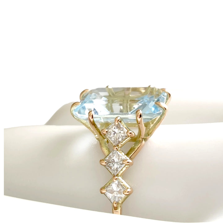 Close-up of a handcrafted 14K yellow gold ring with a large aquamarine and diamond accents, displayed on a white mannequin finger