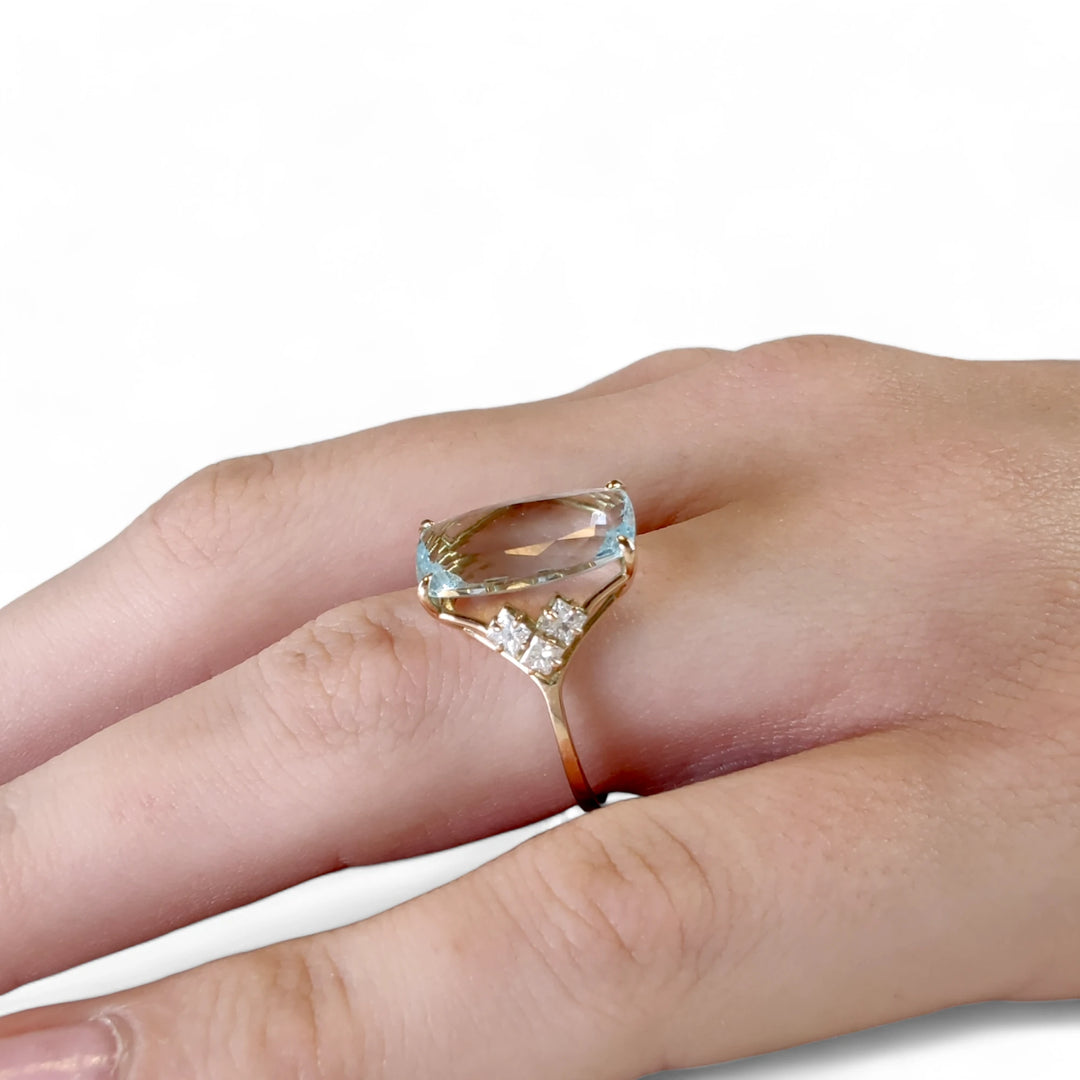 Close-up lateral view of a women’s 14K yellow gold ring featuring a rectangular aquamarine centerpiece and diamonds, displayed on a model’s hand