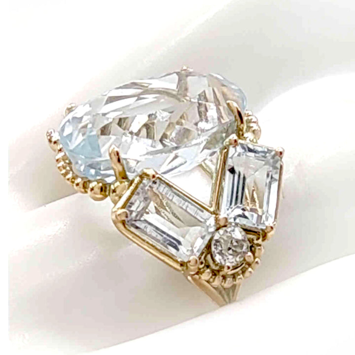 Close-up detail of a unique vintage-style cocktail ring with an oval aquamarine, emerald-cut aquamarines, and diamonds, displayed on a mannequin hand