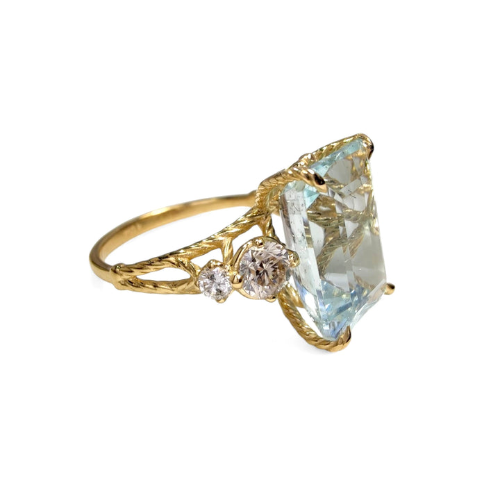 Left side variant view of a cocktail ring in 18K yellow gold with an emerald-cut aquamarine, diamond accents, and a twisted band design