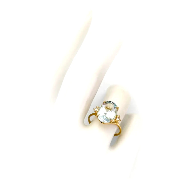 Top view of a women’s 18K yellow gold engagement ring featuring an oval aquamarine centerpiece and two brilliant-cut diamonds displayed on a mannequin hand